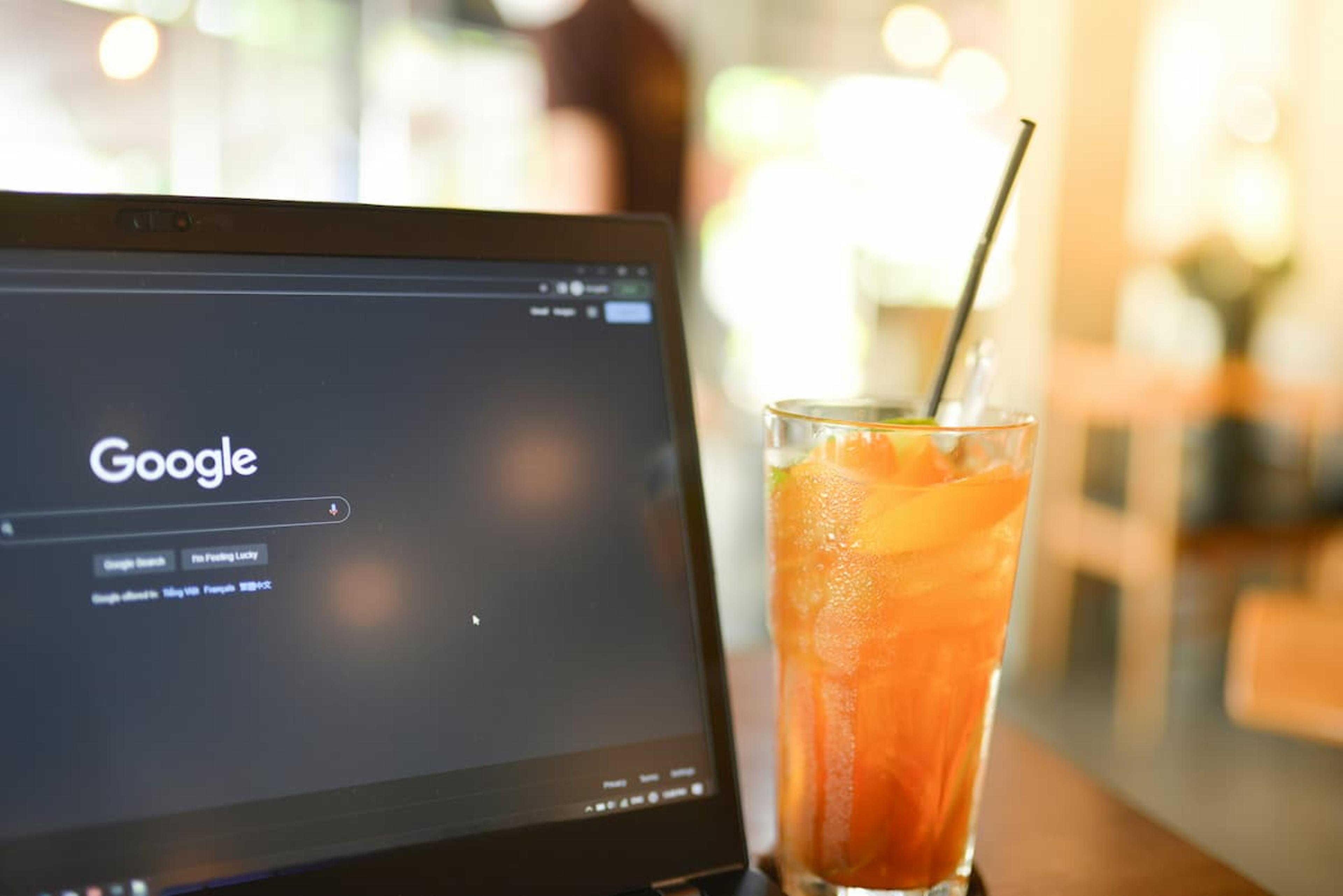 A laptop with a Google browser opened, with a beverage on the side.