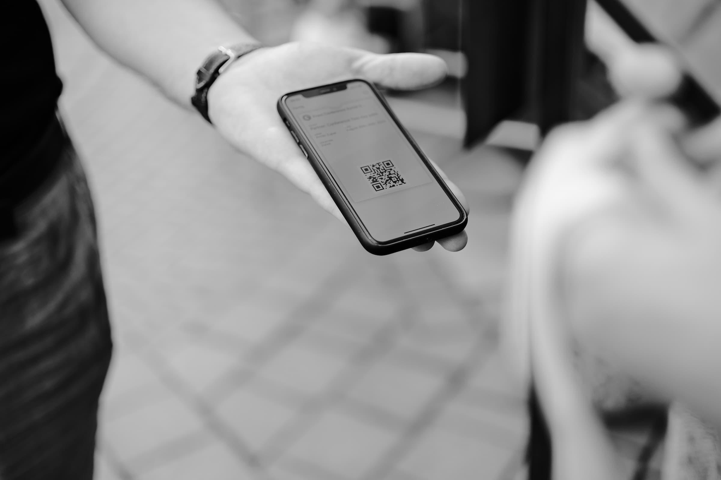 Person holding a mobile phone with a QR code displayed on a screen.